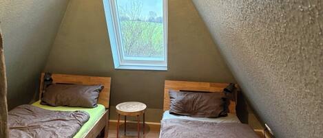 Pieni, kolmionmuotoinen huone, jossa on kaksi sänkyä, pieni pöytä ja ikkuna, josta on näkymä ulos.