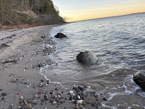 Uma praia com pedras e rochas, uma rocha grande na água e um penhasco com árvores.