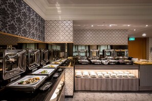Ein reichhaltiges Buffet mit mehreren Speiseausgaben, darunter Tabletts und Schalen, sowie eine Theke mit gestapelten Tellern.