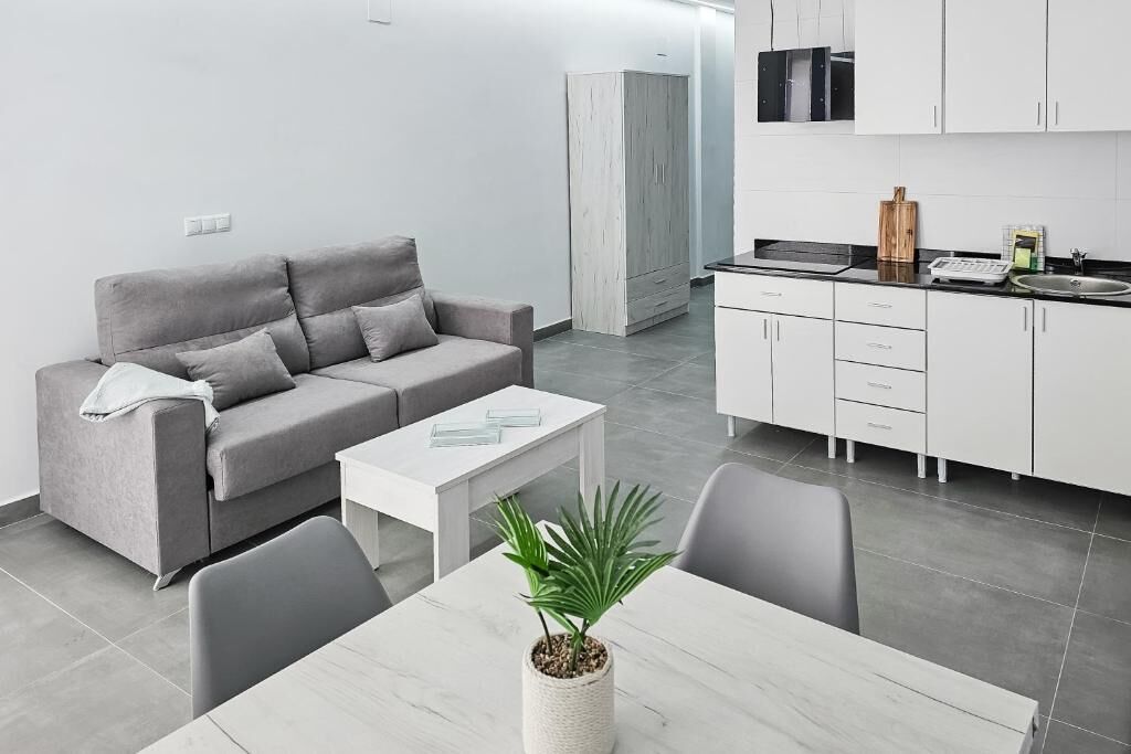 A modern, minimalist living room with a grey sofa, a small white table, and a potted plant.