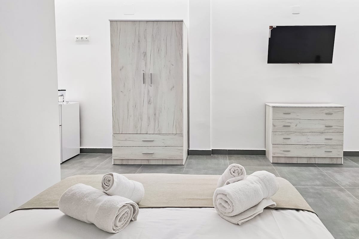 A modern bedroom with a bed, two white dressers, a wardrobe, and a flat-screen TV.