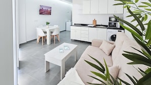 A modern kitchen with white cabinets, a dining area with a white table and chairs, and a beige sofa. - Ros Lil Suites (Alicante)