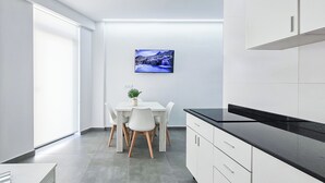 A modern kitchen with white cabinets, a black countertop, and a dining area with a white table and chairs. - Ros Lil Suites (Alicante)