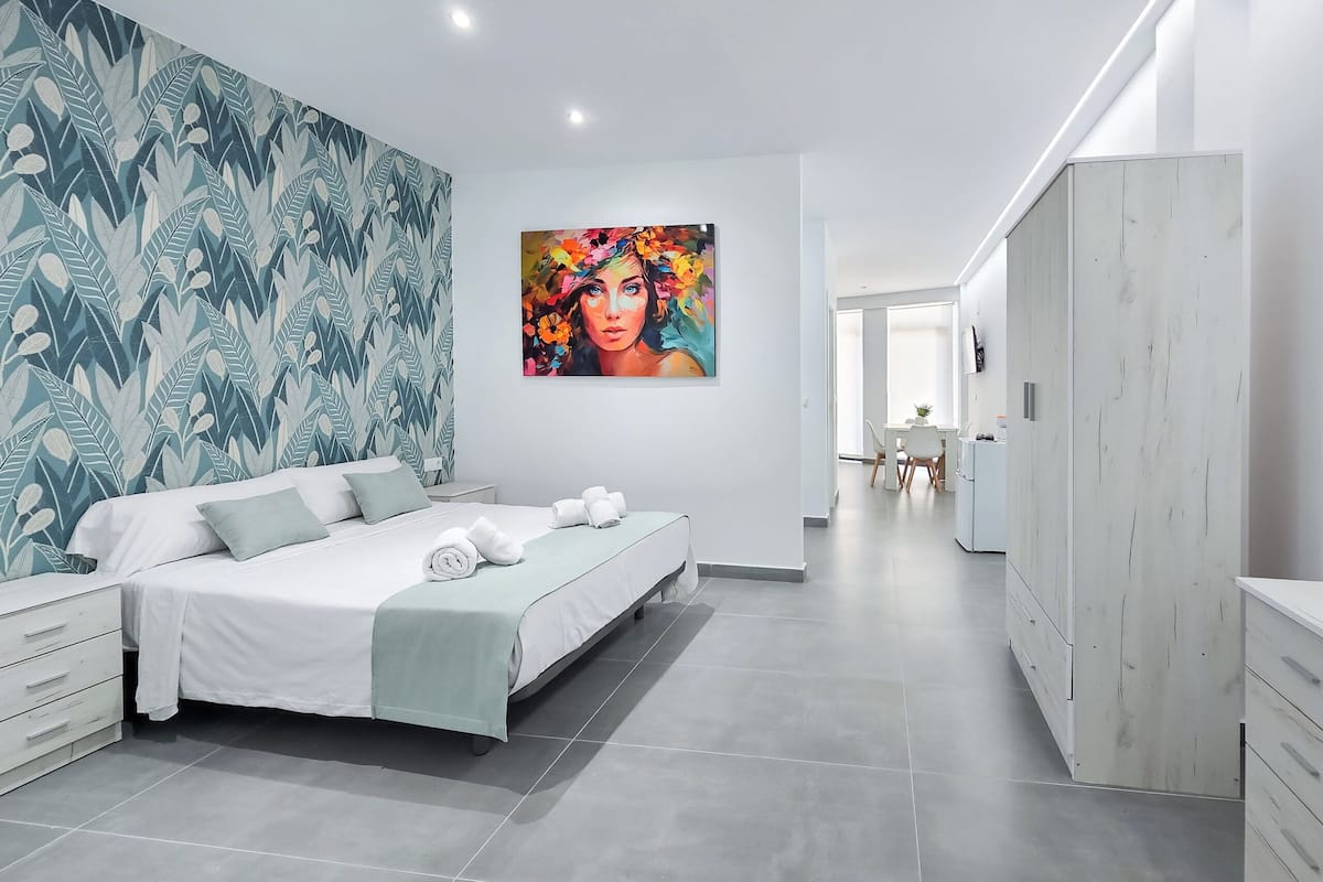 A modern bedroom with a large bed, a wardrobe, and a painting on the wall.
