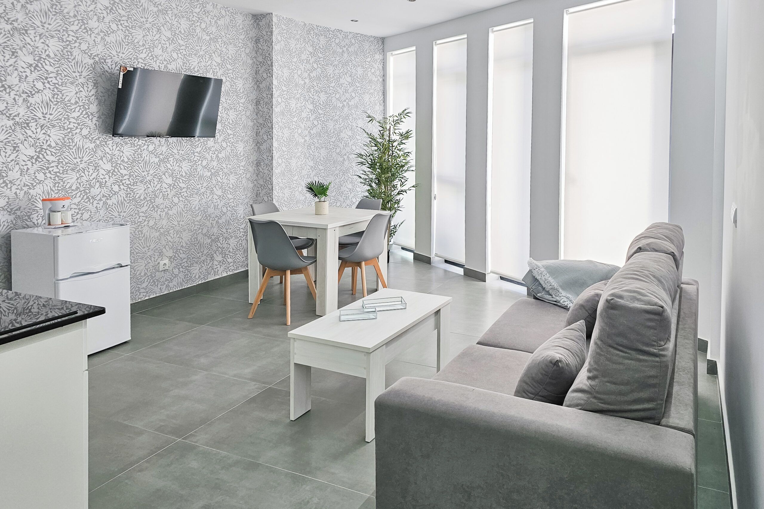 Ein modernes Wohnzimmer mit einem grauen Sofa, einem weißen Couchtisch und einem Essbereich mit Tisch und Stühlen.