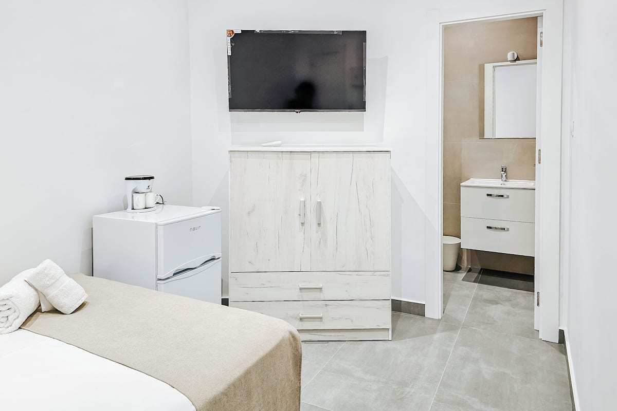 A modern hotel room with a bed, a TV mounted on the wall, a wardrobe, and a bathroom with a mirror and sink.