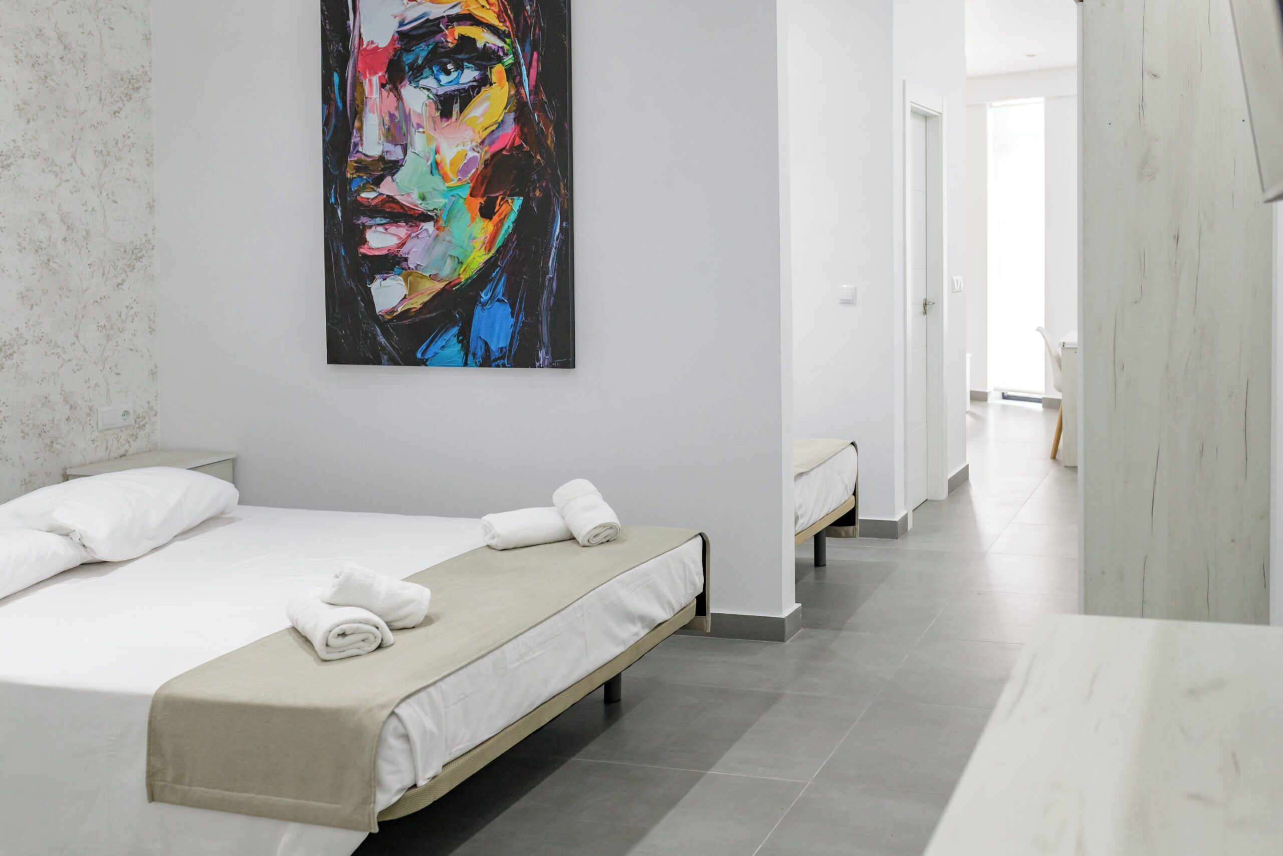 A hotel room with two beds, a large abstract painting on the wall, and a view of the hallway.