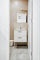 Un baño estrecho con tocador blanco, espejo y retrete.