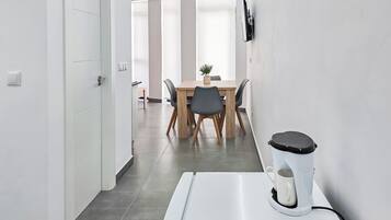 Quarto de hotel moderno com área de refeições, mesa e cadeiras de madeira, uma planta em vaso e uma cafeteira.
