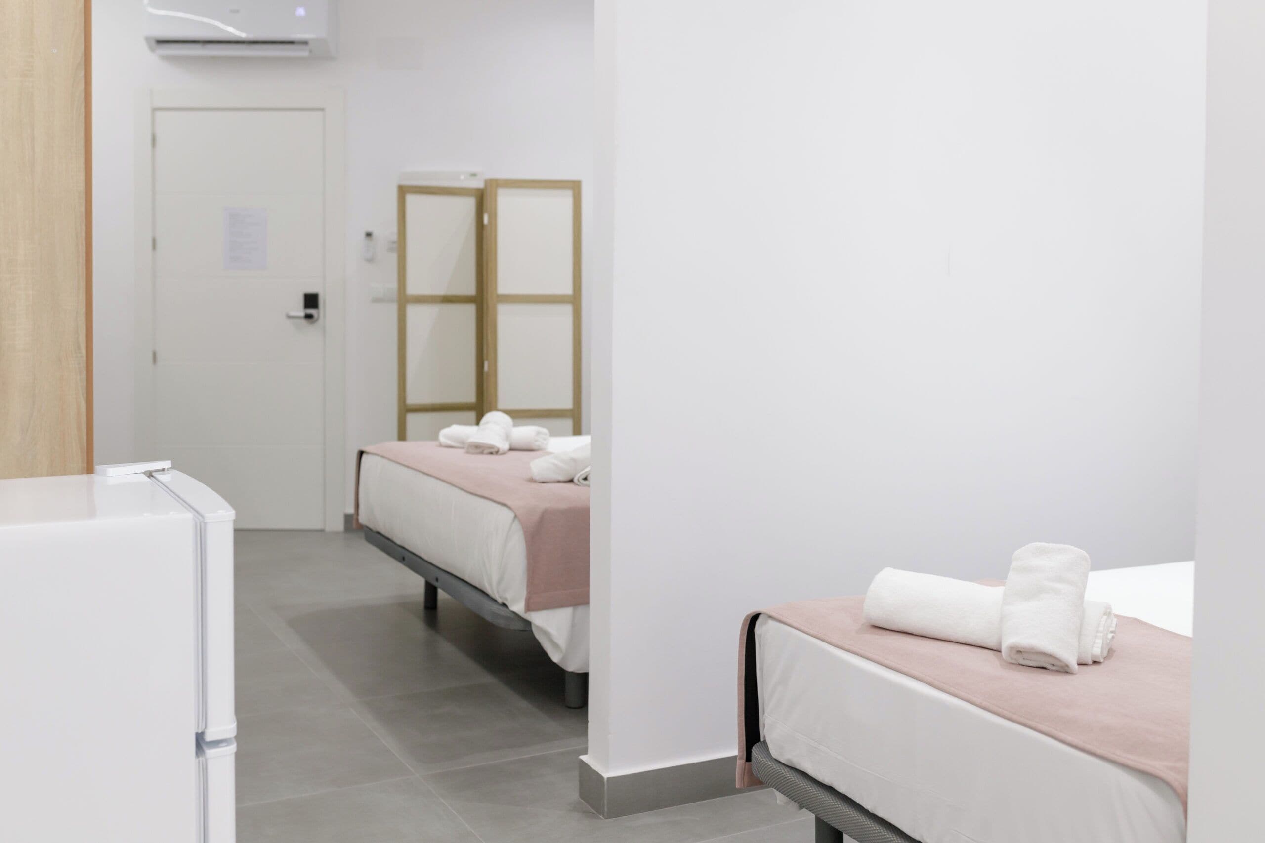 Hotellihuone, jossa on sänky, yöpöytä, peili ja ovi.