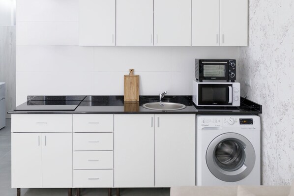 Une cuisine compacte avec des meubles blancs, un plan de travail noir, un four à micro-ondes, un grille-pain et un lave-linge.