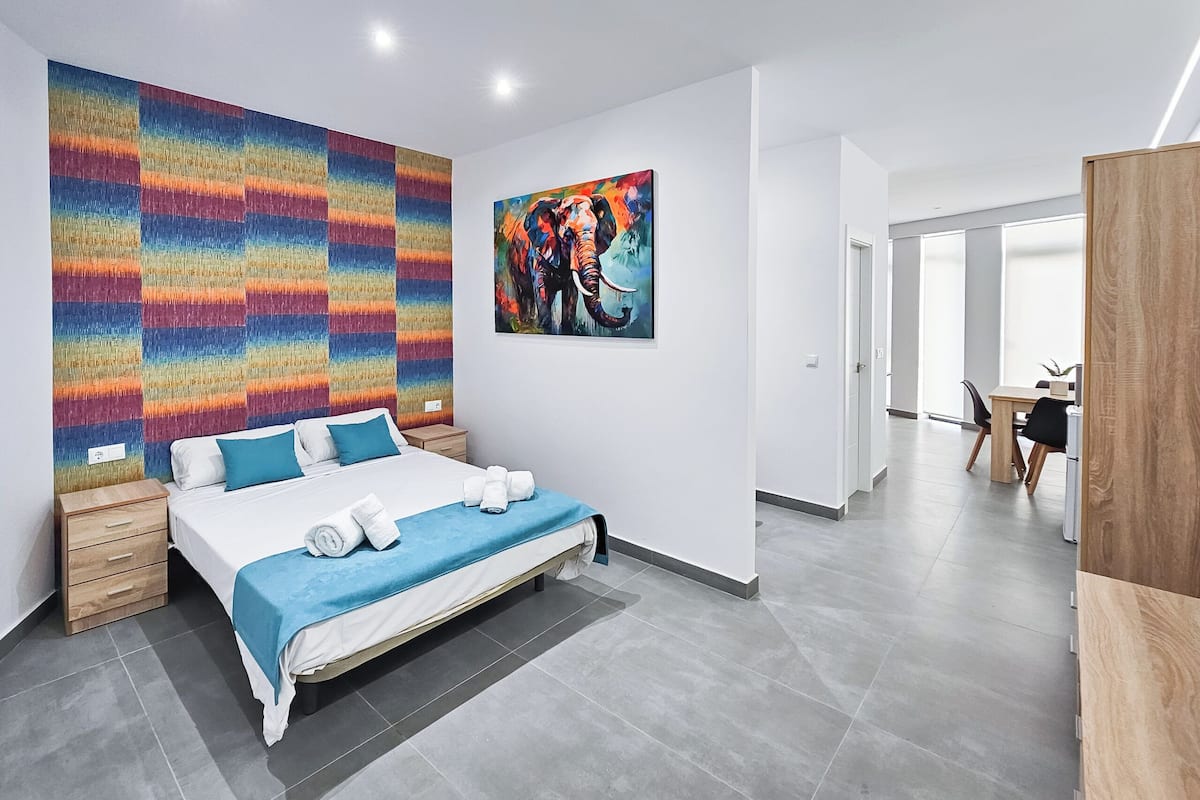A modern hotel room with a large bed, a colorful abstract painting, and a view of the hallway.