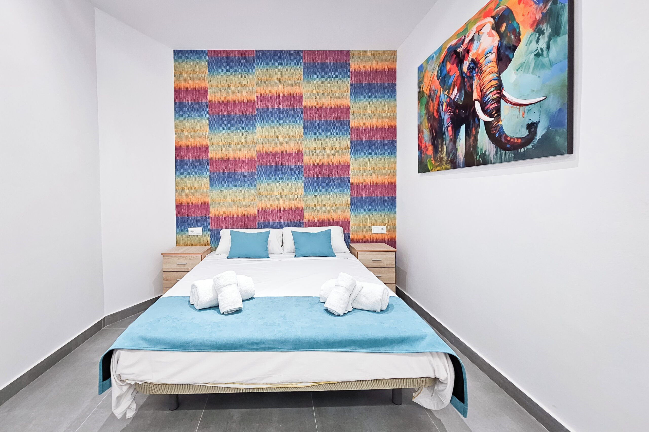 A hotel room with a bed, a colorful abstract wall art, and a painting of an elephant.