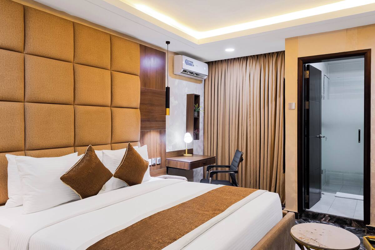 A hotel room with a large bed, a desk, a chair, and a door leading to a balcony.