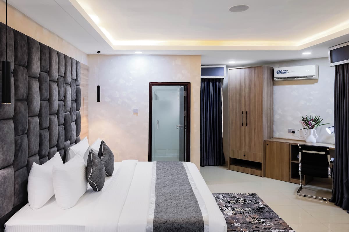 A modern bedroom with a large bed, a tufted headboard, a desk, and an air conditioning unit.