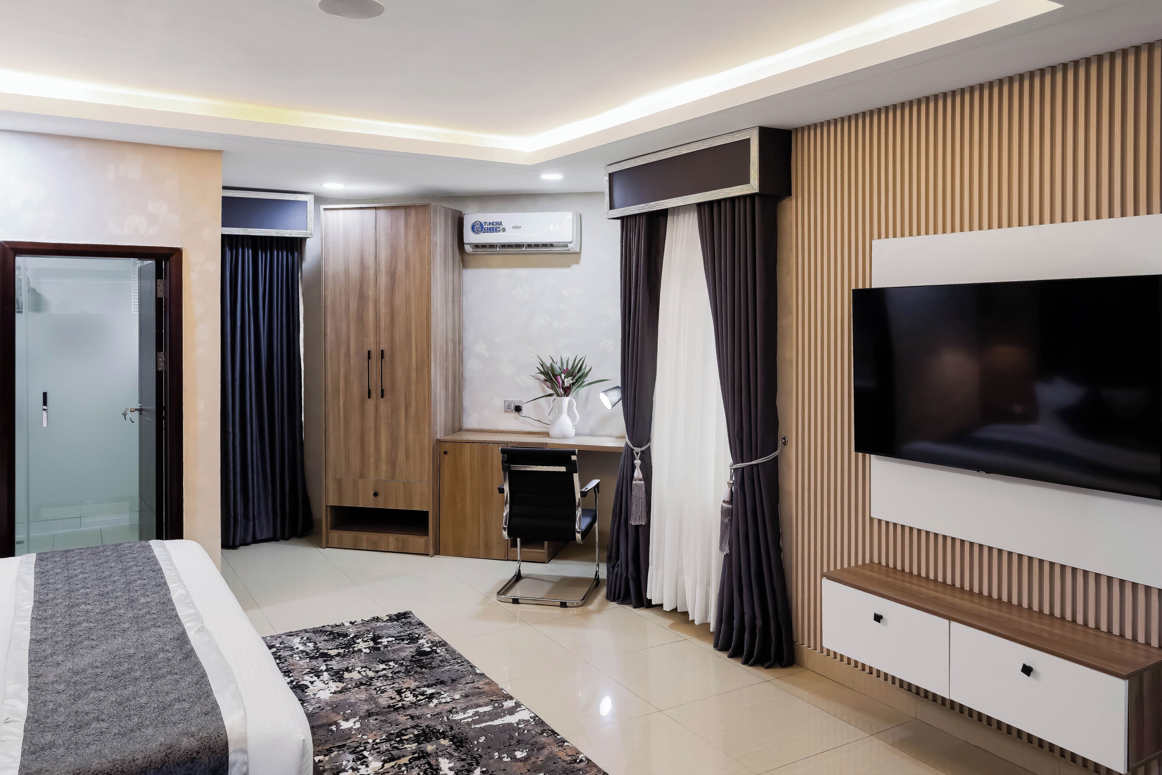 A modern hotel room with a bed, a desk, a TV, and a wardrobe.