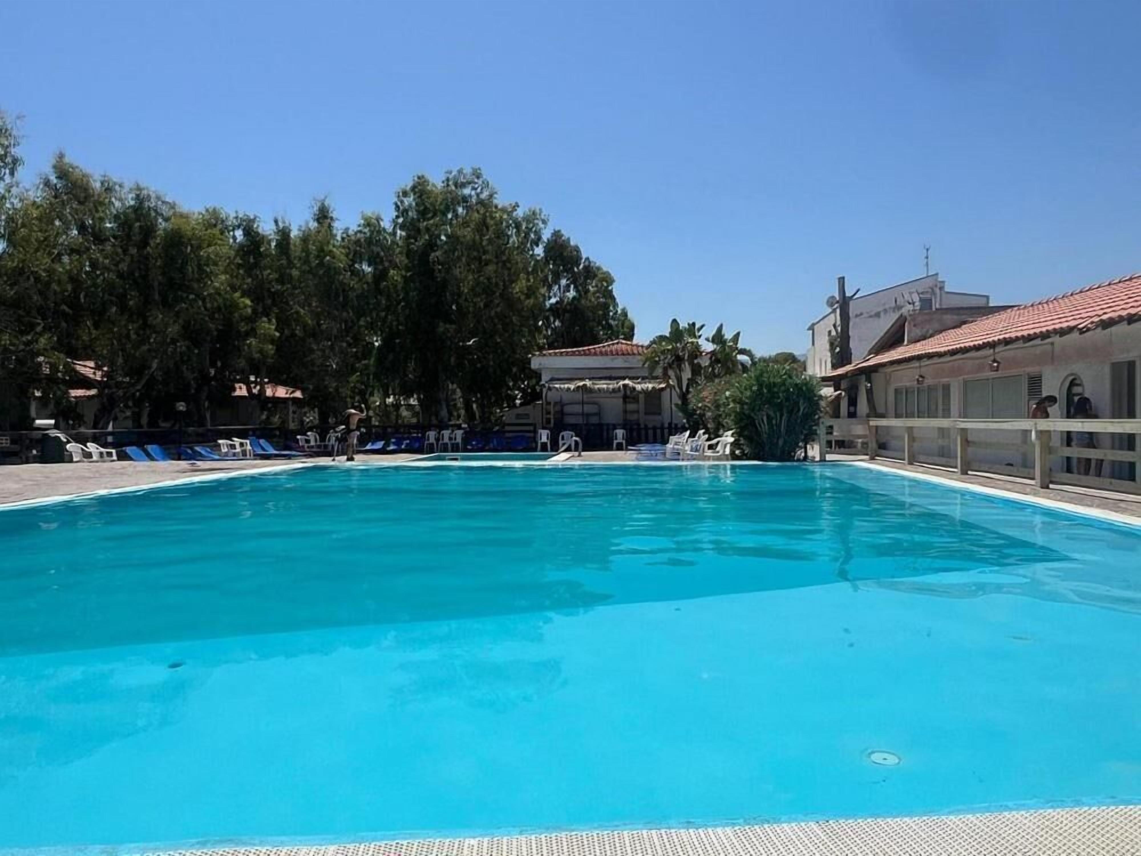 Ein Schwimmbecken mit klarem, blauem Wasser, umgeben von Liegestühlen und Palmen.