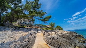 Une propriété située sur la côte, avec un sentier rocheux menant à une maison, entourée d’arbres et offrant une vue sur la mer.
