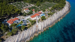 Vue aérienne d’une propriété située sur la côte, comprenant plusieurs bâtiments, une piscine et une plage rocheuse.