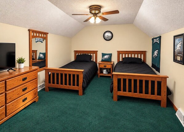 A bedroom with two wooden beds, a dresser, a ceiling fan, and Eagles-themed decorations.