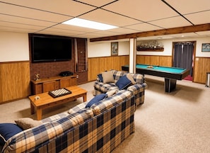 A room with a pool table, a sofa set, a television, and a wooden cabinet.