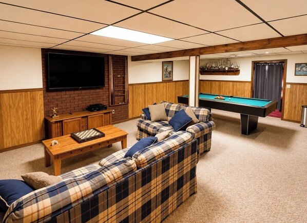 A room with a pool table, a sofa set, a television, and a wooden cabinet.