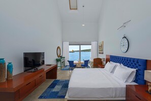 A hotel room with a bed, a TV, a desk, and a view of the sea.
