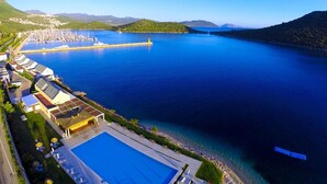 An aerial view of a coastal hotel with a large swimming pool, a marina with boats, and a mountainous backdrop. - The Doria Yacht Club Kas Hotel (Kaş)