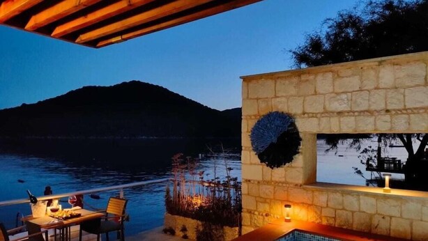 An outdoor pool area with a stone wall, a table with chairs, and a view of a body of water and hills. - The Doria Yacht Club Kas Hotel (Kaş)