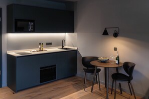 A modern kitchen with dark cabinetry, a built-in microwave, a sink, and a dining area with two chairs and a table. - Conlon House Central (Munich)