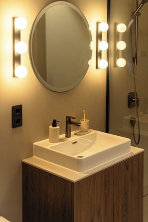 A bathroom with a vanity, a mirror with lights, a soap dispenser, and a toothbrush holder. - Conlon House Central (Munich)