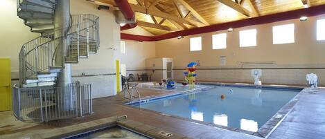 Una piscina interior con una escalera en espiral, un tobogán de agua y un aro de baloncesto.