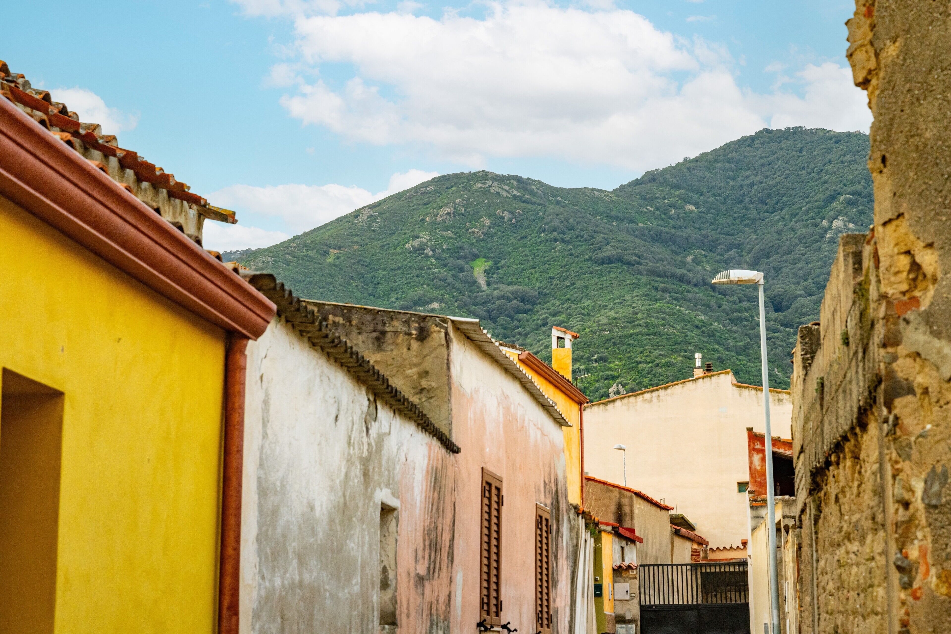 Uma rua estreita com edifícios, uma montanha ao fundo e um poste de luz.