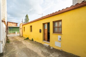 A narrow alleyway leading to a yellow building with a wooden door and windows.