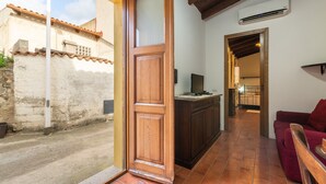 Una puerta de madera abierta que da a una cocina con suelo de baldosas, un sofá rojo y un equipo de aire acondicionado en la pared.