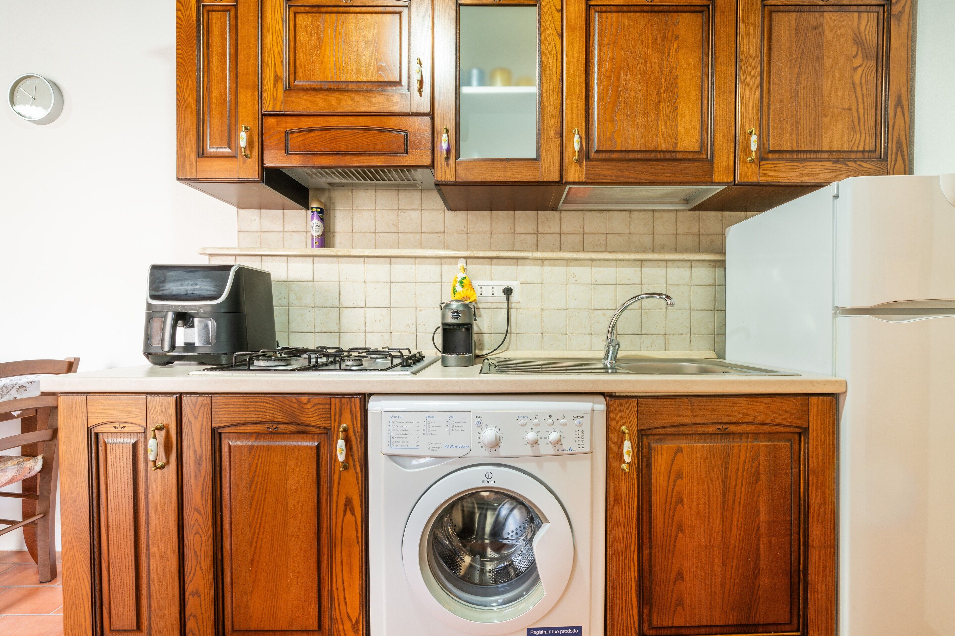 Una cocina con armarios de madera, lavadora, cafetera y estufa.