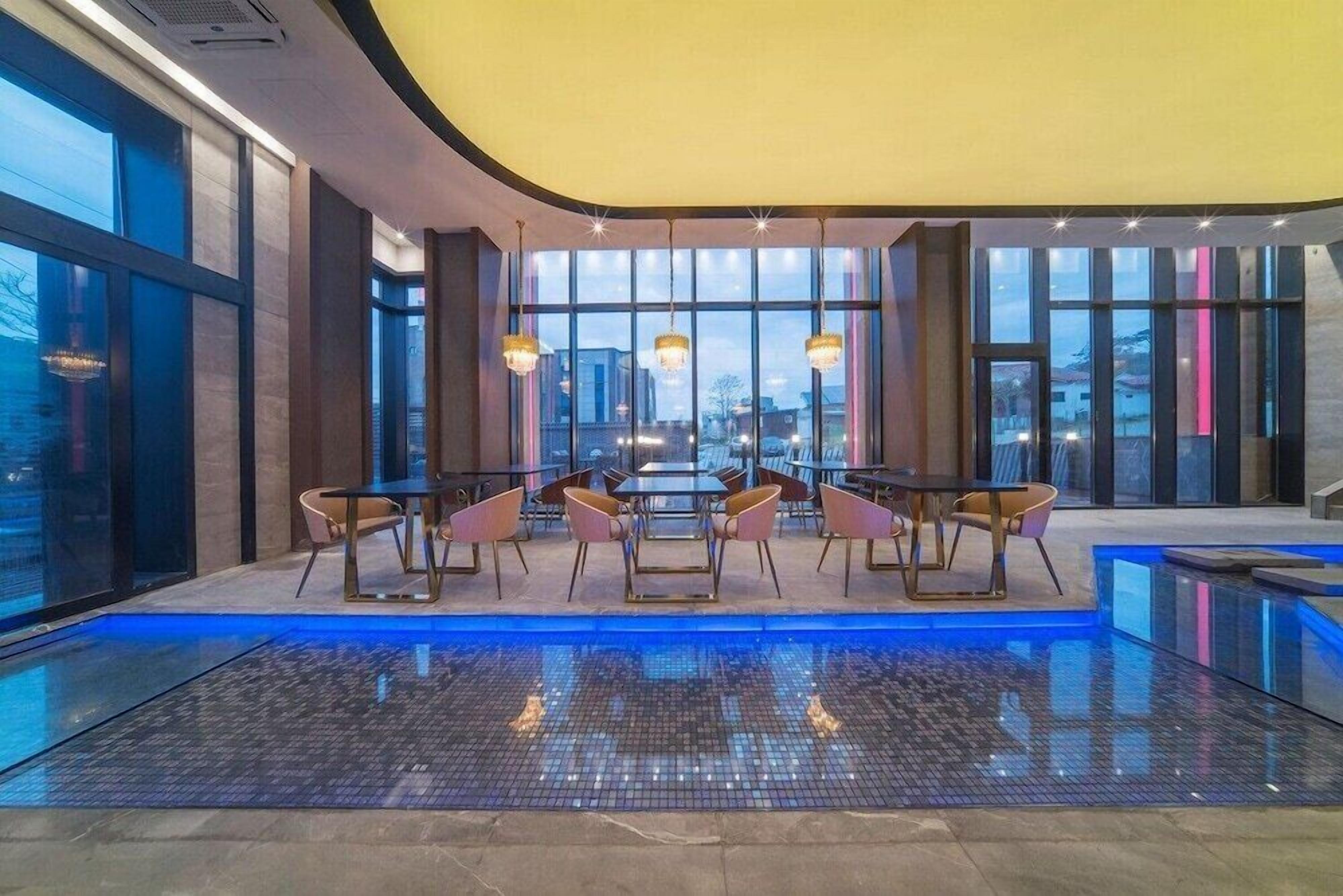 Un área de piscina interior moderna con zona de comedor y ventanas amplias.