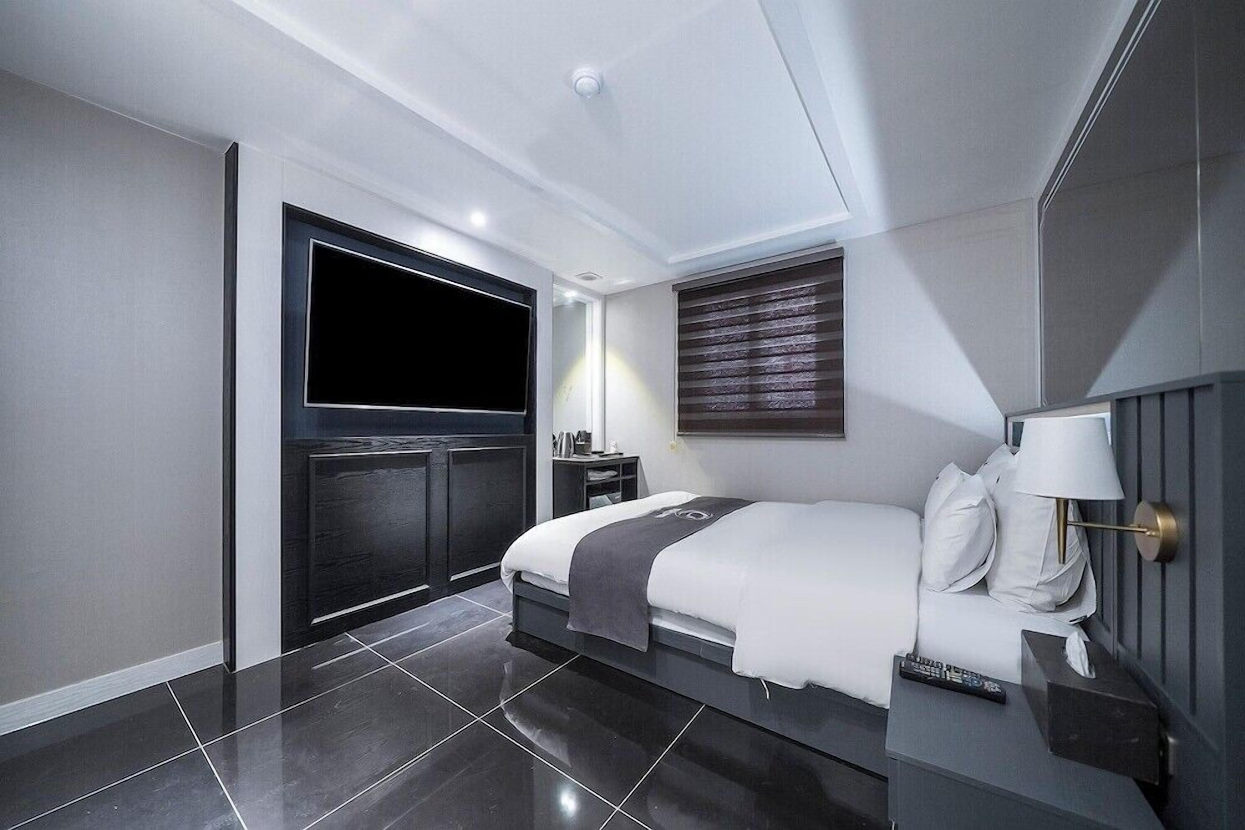 Una habitación de hotel moderna con una cama grande, una mesita de noche con lámpara, un televisor montado en la pared y una puerta corredera.
