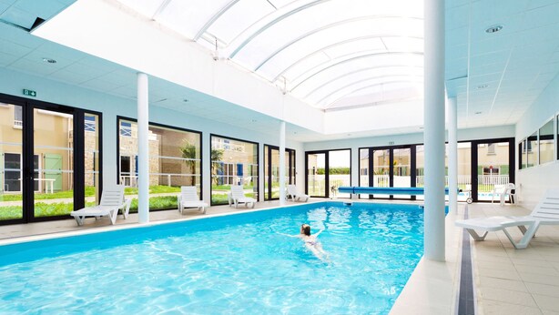 Ein Innenpool mit klarem, blauem Wasser, umgeben von Liegestühlen und einer Glaskuppel.