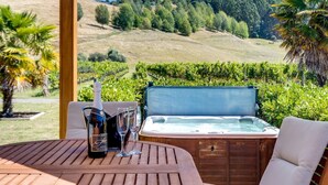 A wooden table with a bottle of wine, two glasses, and a hot tub in a scenic outdoor setting. - The Farmhouse At Mission Estate (Napier)