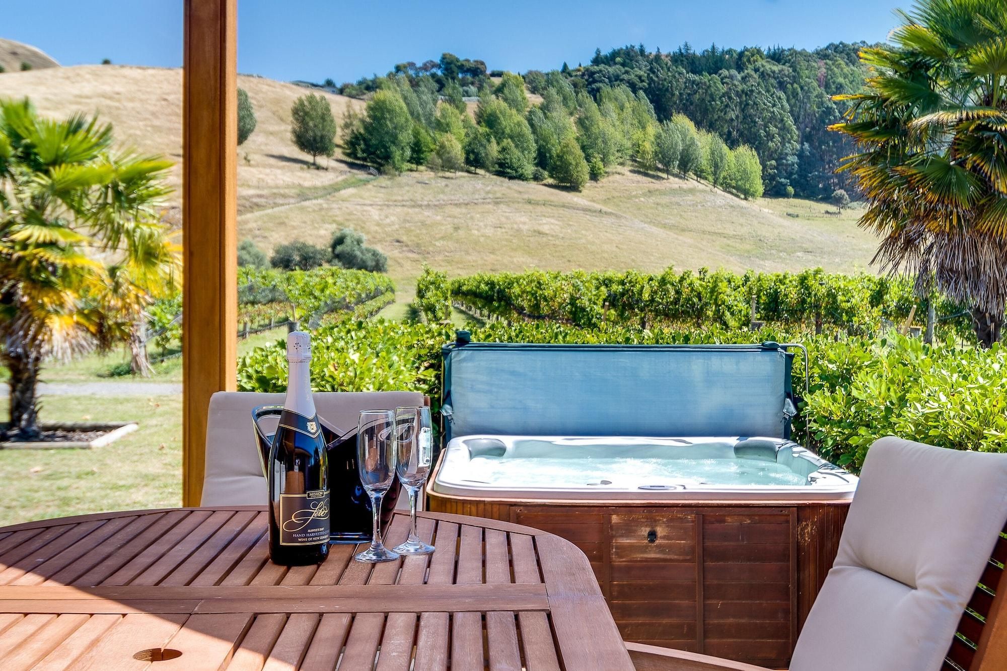 Una mesa de madera con una botella de vino, dos copas y un jacuzzi en un entorno natural pintoresco.