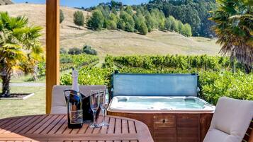 Una mesa de madera con una botella de vino, dos copas y un jacuzzi en un entorno natural pintoresco.