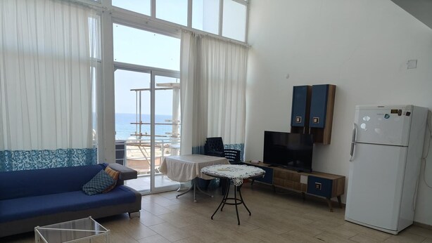 A compact living space with a sofa, a small dining table, a TV, and a refrigerator. - 2-bedroom apartment in perfect Erdemli with air conditioning (Erdemli)