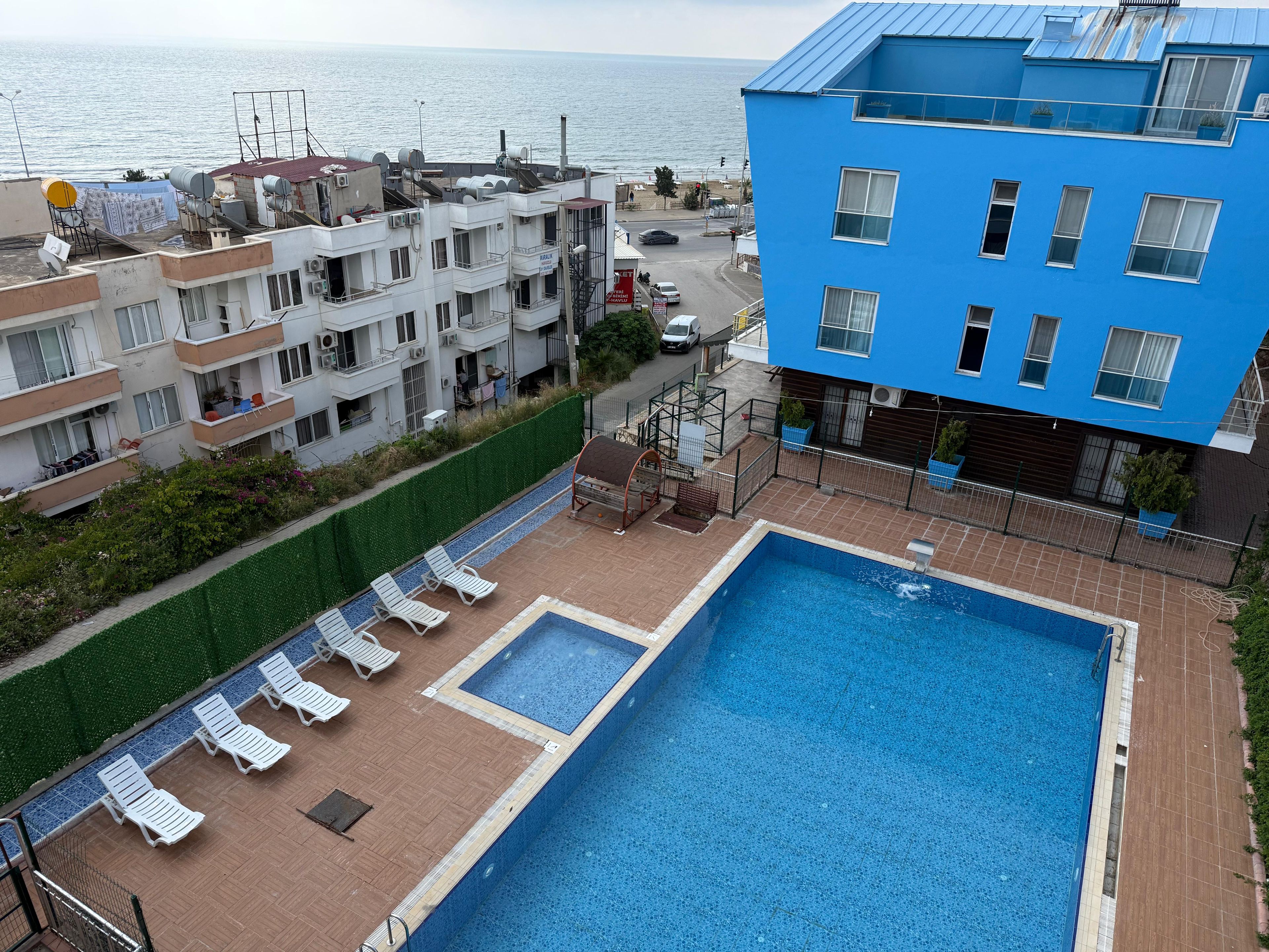 Ein Dachpool mit Liegestühlen, Blick aufs Meer und angrenzende Wohnhäuser.