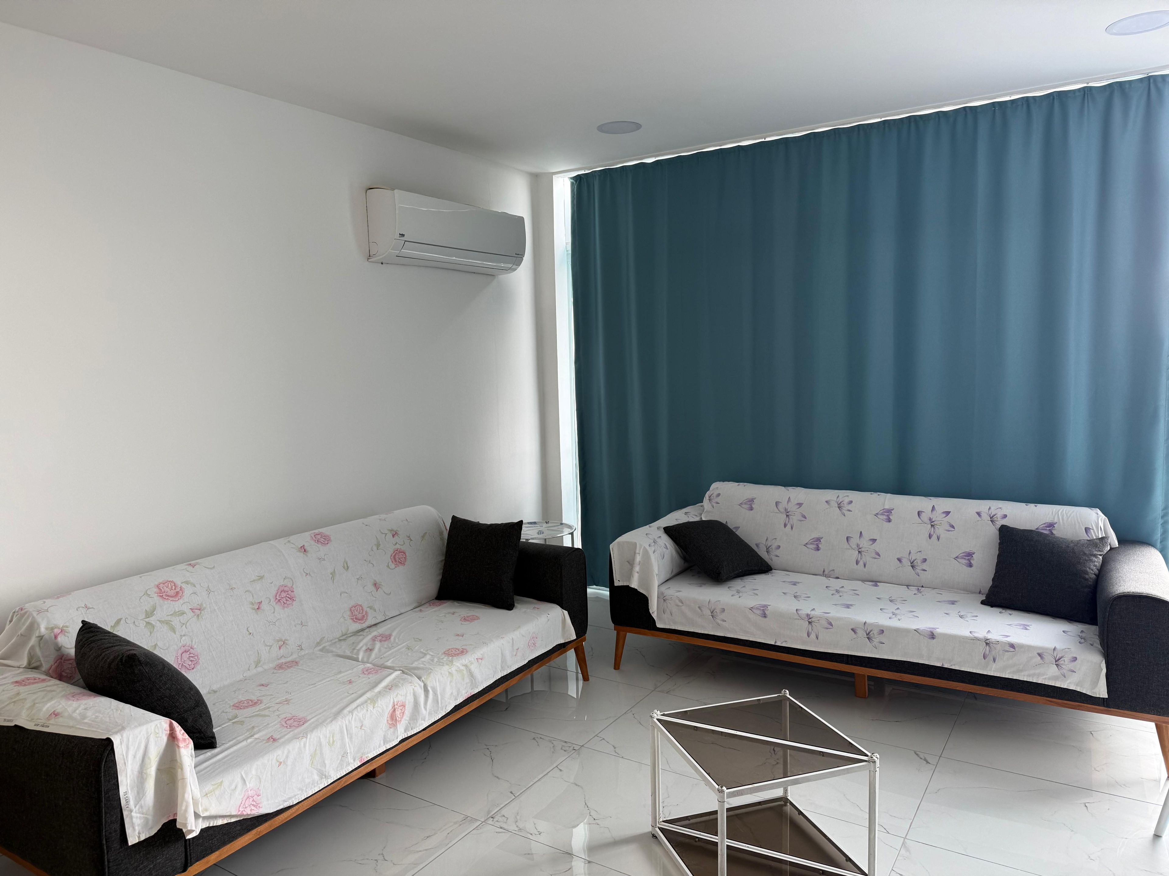 Ein modernes Wohnzimmer mit zwei Sofas, einem kleinen Tisch und einem großen Fenster mit Vorhängen.