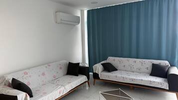 Ein modernes Wohnzimmer mit zwei Sofas, einem kleinen Tisch und einem großen Fenster mit Vorhängen.