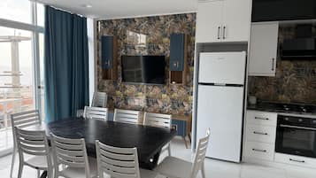 Una cuina moderna amb televisió de pantalla plana, armaris blancs i zona de dinar amb taula negra i cadires blanques.