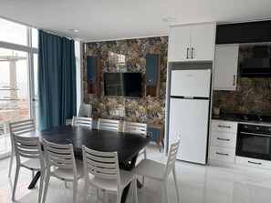 A modern kitchen with a flat-screen TV, white cabinets, and a dining area with a black table and white chairs.