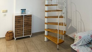 A compact room with a spiral staircase, a small wooden cabinet, and a bed with floral bedding. - 2-bedroom apartment in perfect Erdemli with air conditioning (Erdemli)