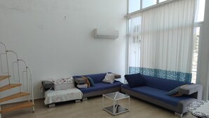 A living room with a blue sofa set, a small table, a staircase, and a large window with sheer curtains. - 2-bedroom apartment in perfect Erdemli with air conditioning (Erdemli)